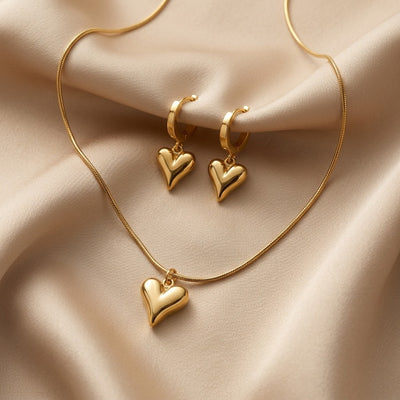 Gold heart-shaped necklace and earrings on a beige fabric background