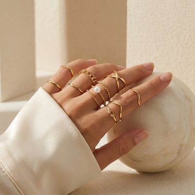 Hand wearing multiple gold rings with a marble sphere in the background