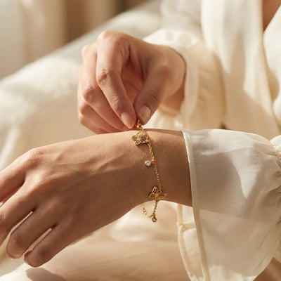 Person wearing a gold bracelet with a delicate design, set against a soft, neutral background.