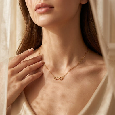 Woman wearing a gold necklace with an infinity symbol, held by a hand.
