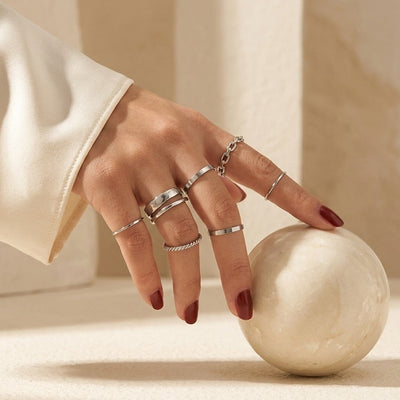 Hand with multiple silver rings on a neutral background