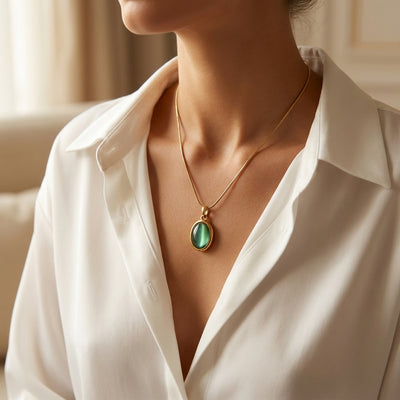Person wearing a white shirt with a gold necklace featuring a green pendant.