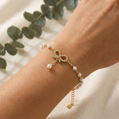 Gold bracelet with pearl beads on a wrist, with green leaves in the background