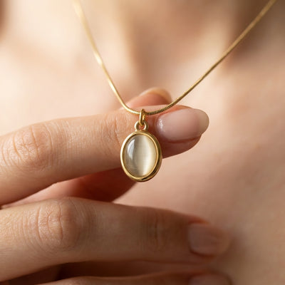 Gold necklace with a pendant held by a hand against a blurred background